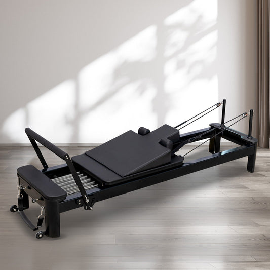 A black Pilates Reformer on a wooden floor.